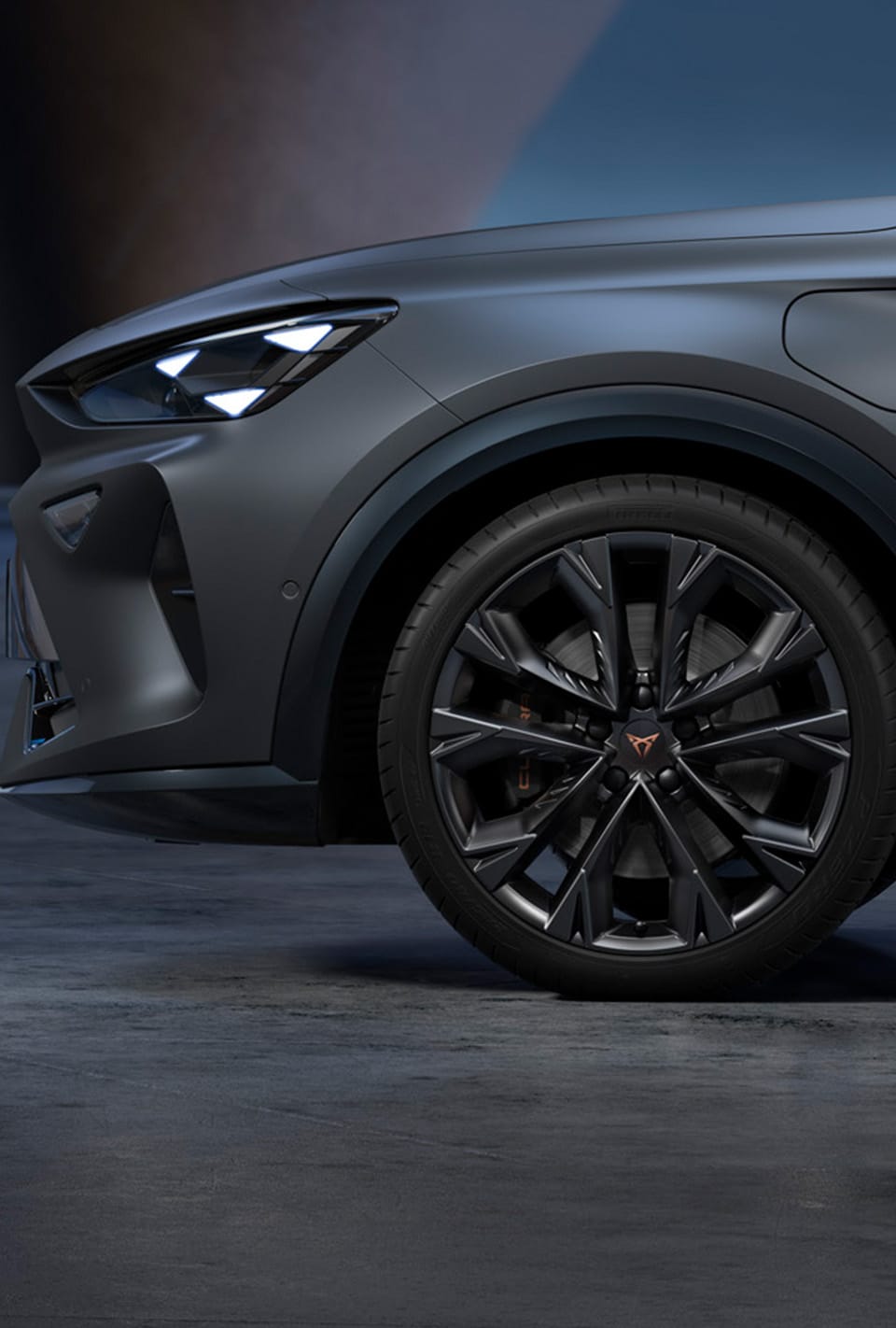Vue en grand angle de la nouvelle CUPRA Leon Sportstourer 2024, véhicule hybride sportif de couleur gris mat, garé dans un environnement urbain, devant de grandes fenêtres géométriques d'inspiration gaudi.