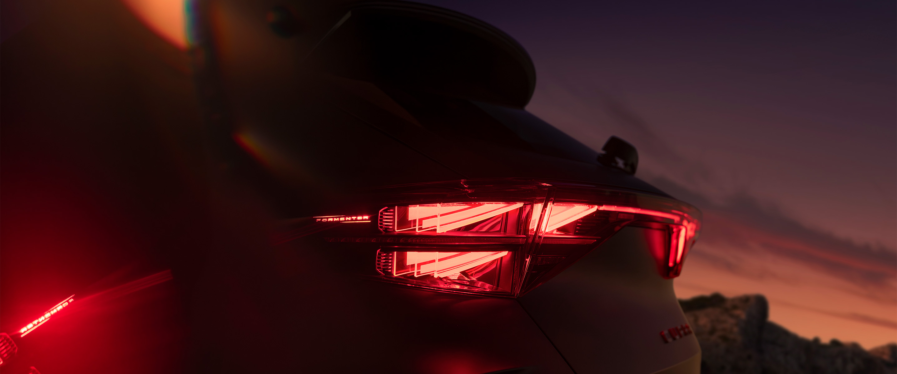 close up of the new cupra formentor's 2024 illuminated rear light showcasing angular design and a red glow against the sunset backround.​