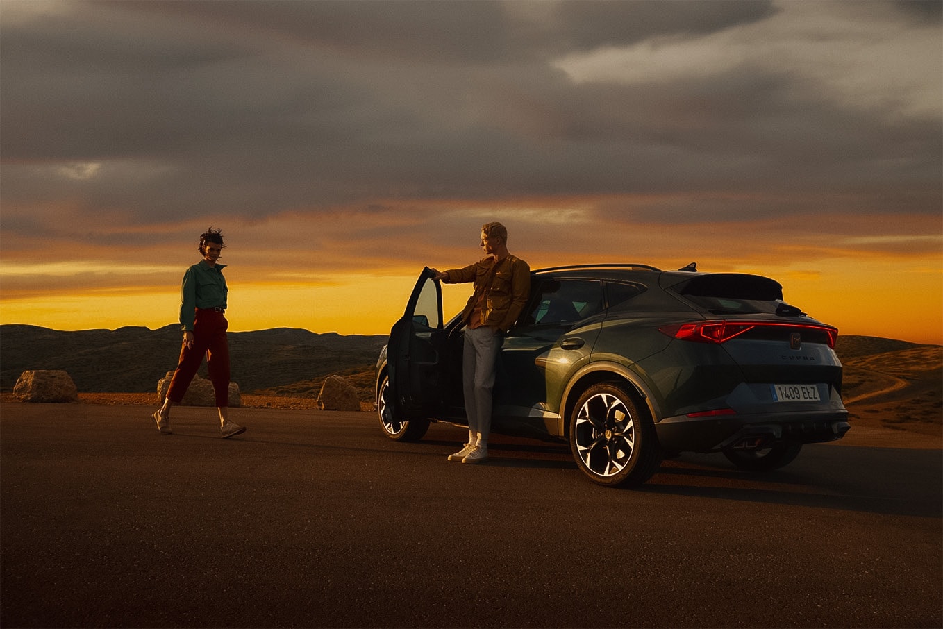 L'homme se tient dans la portière ouverte du conducteur de sa CUPRA et regarde au loin le soleil qui se couche.