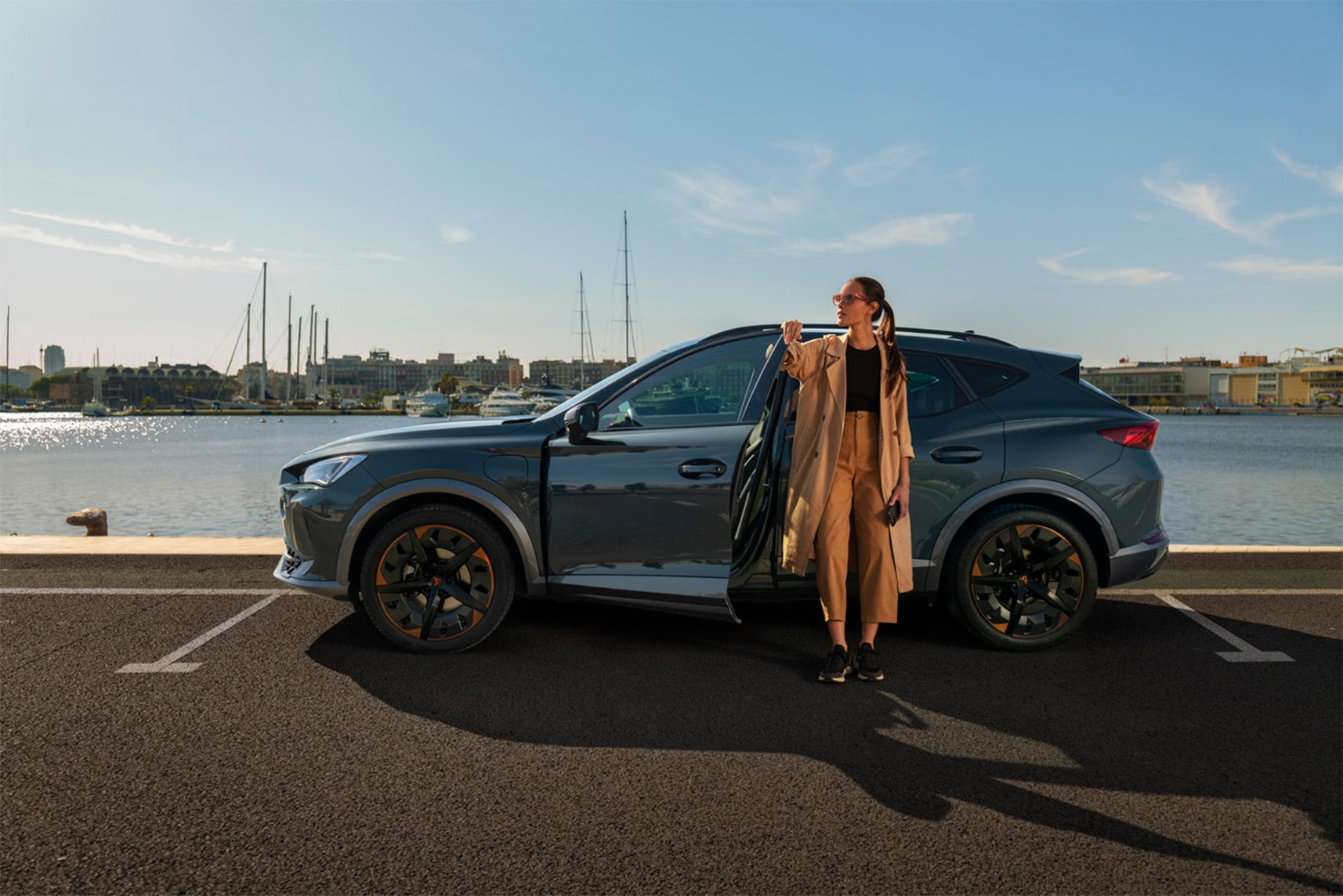 Une femme se tient dans la portière du conducteur de sa CUPRA, garée dans un port urbain.